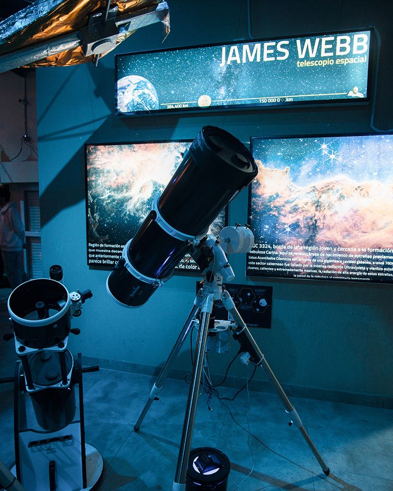 Telescopio frente a una pantalla con imágenes del telescopio espacial James Webb en el Planetario CIASIVE